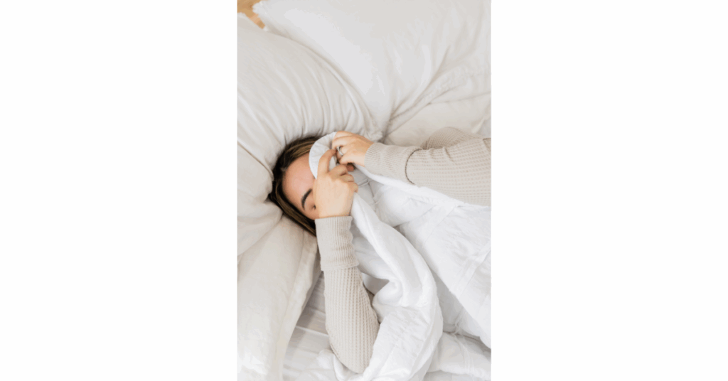 Tired woman in bed covering face with blanket, showing signs of sleep deprivation, insomnia, or obstructive sleep apnea